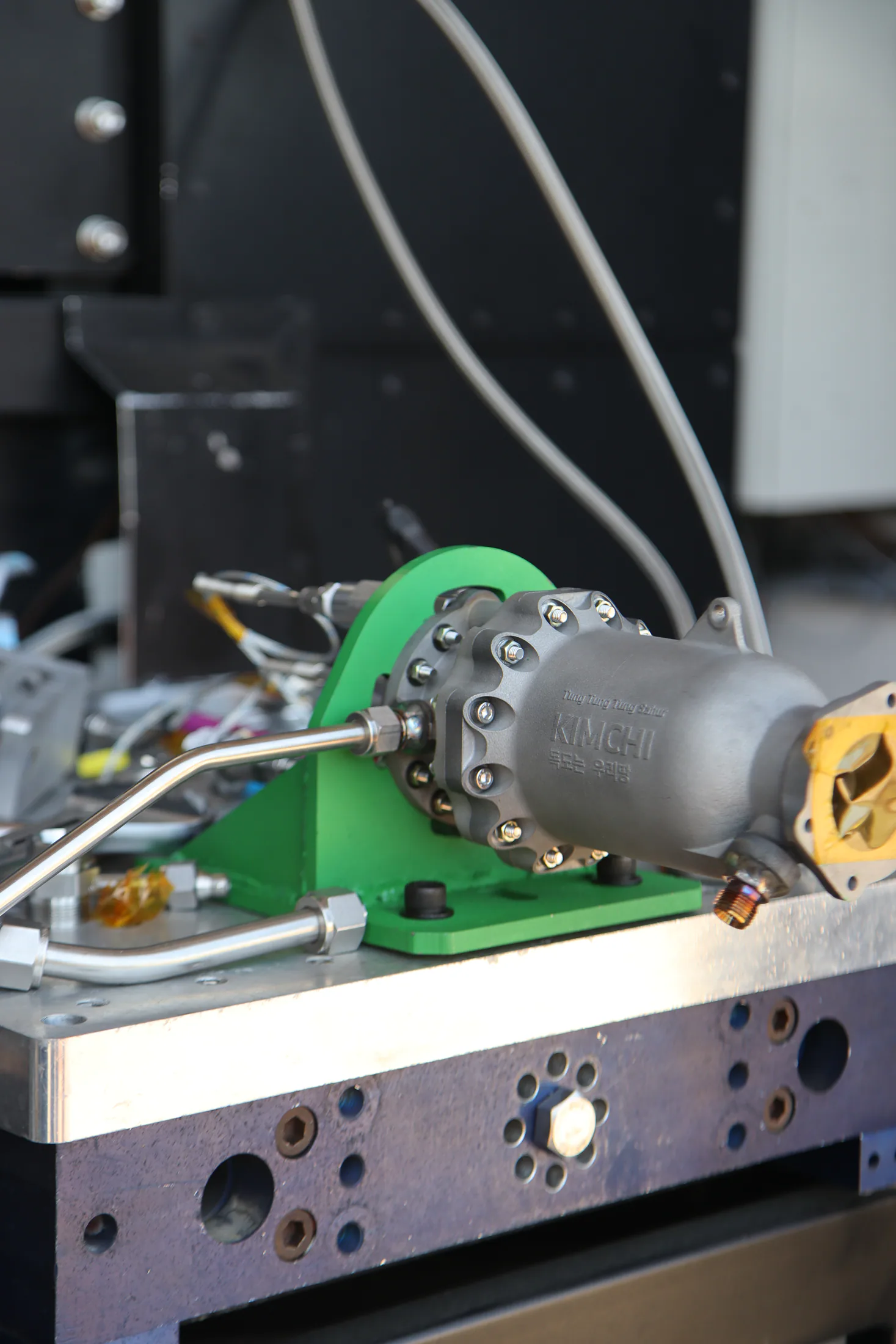 Side view of the cylindrical engine bolted to a green bracket on the facility test table.
