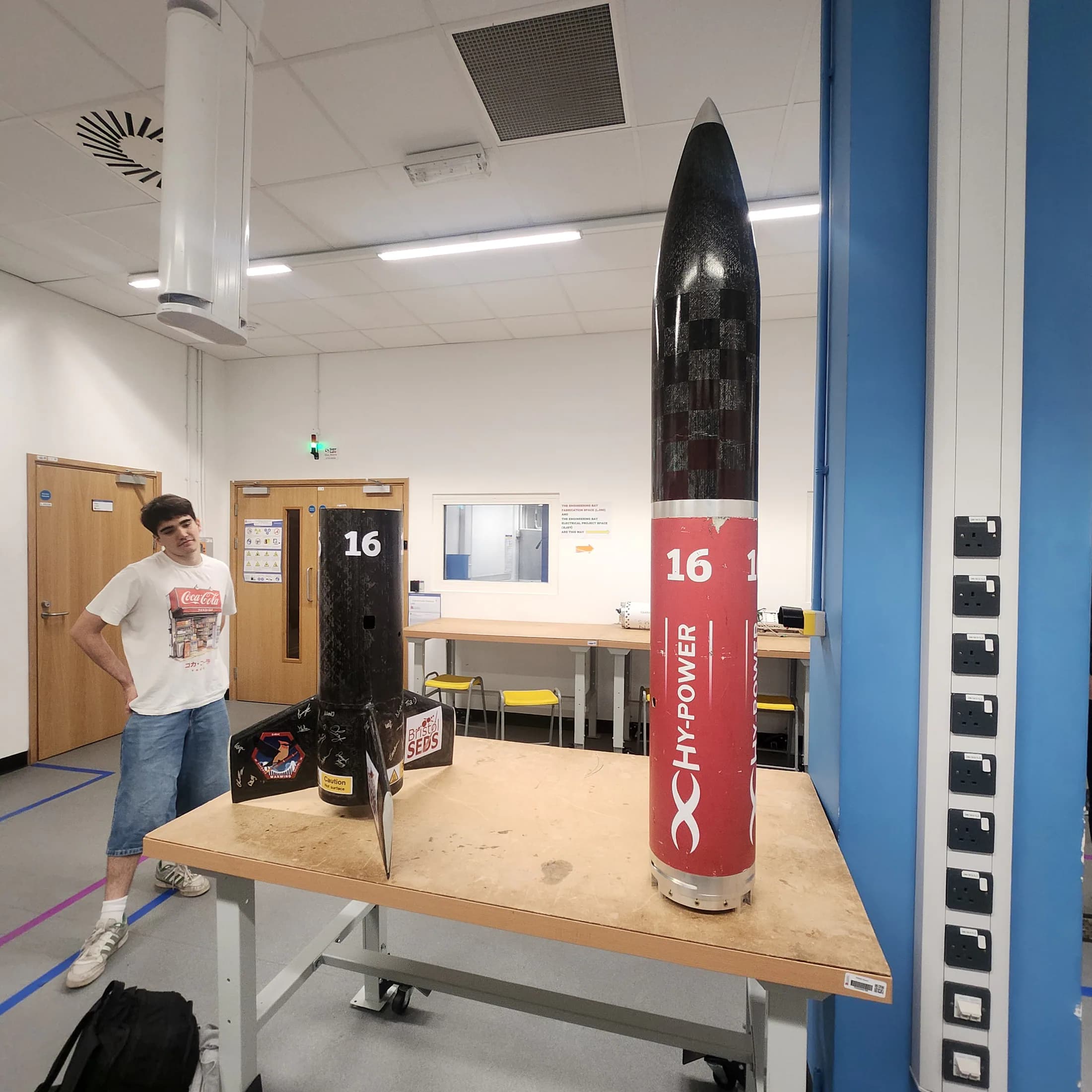 Black-and-red Bristol student rocket standing upright on a table in a laboratory.