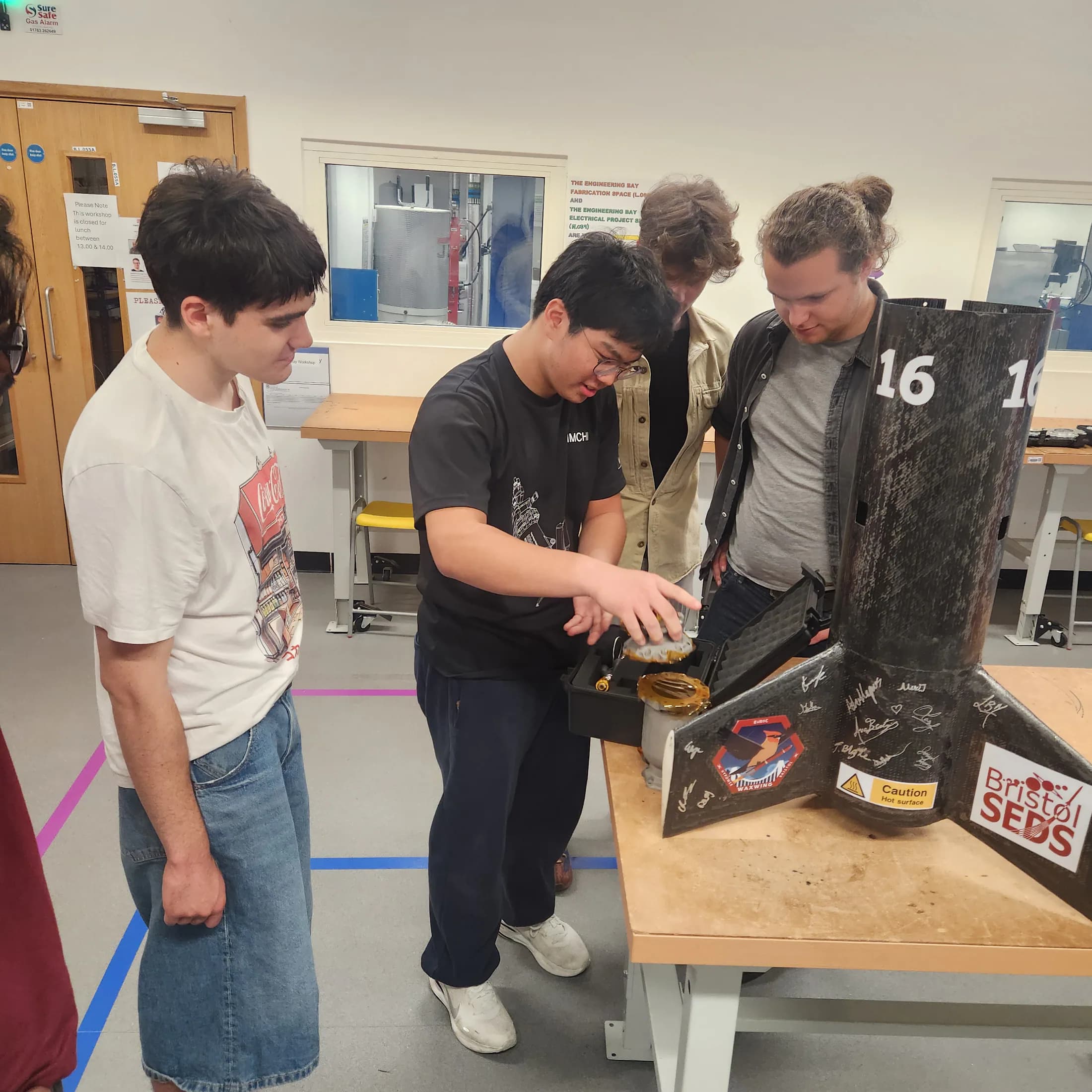 Students gathered around an open rocket section and discussing its internal hardware.