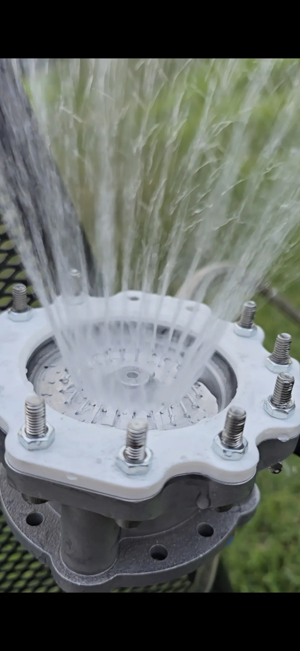 Multiple water streams spreading upward from a circular multi-hole engine component during flow testing.