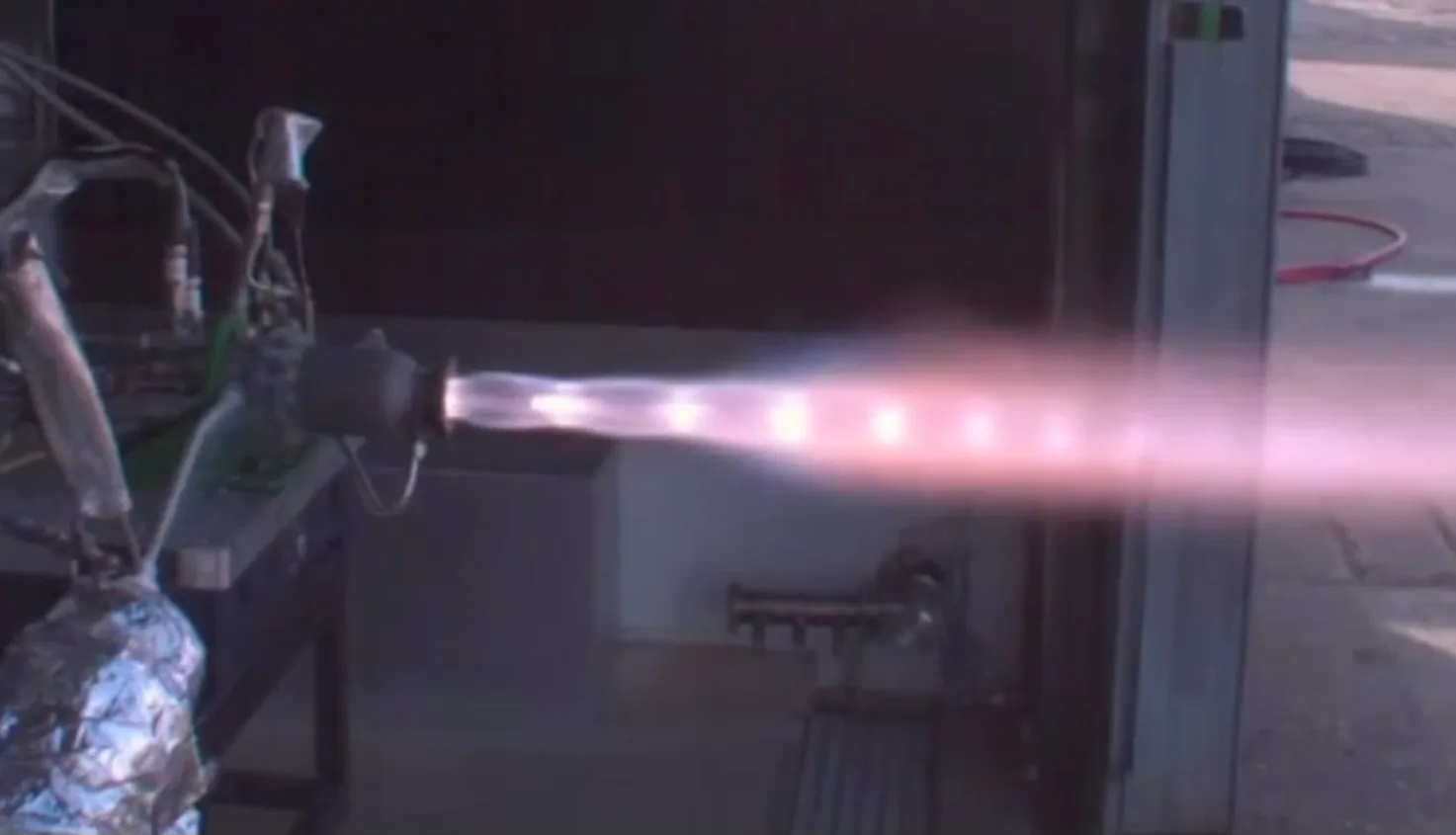 Close-up of the engine nozzle with a bright pink-white exhaust plume extending across the frame.