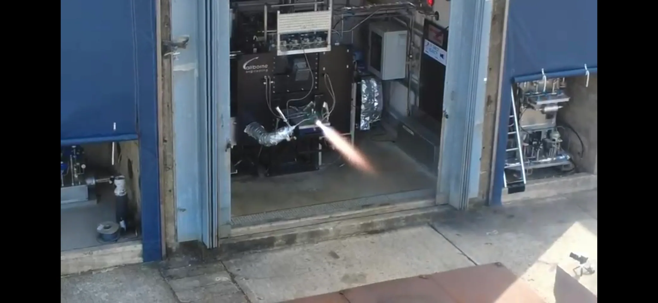 Wide exterior view into the test bay while the rocket engine produces a bright exhaust plume.