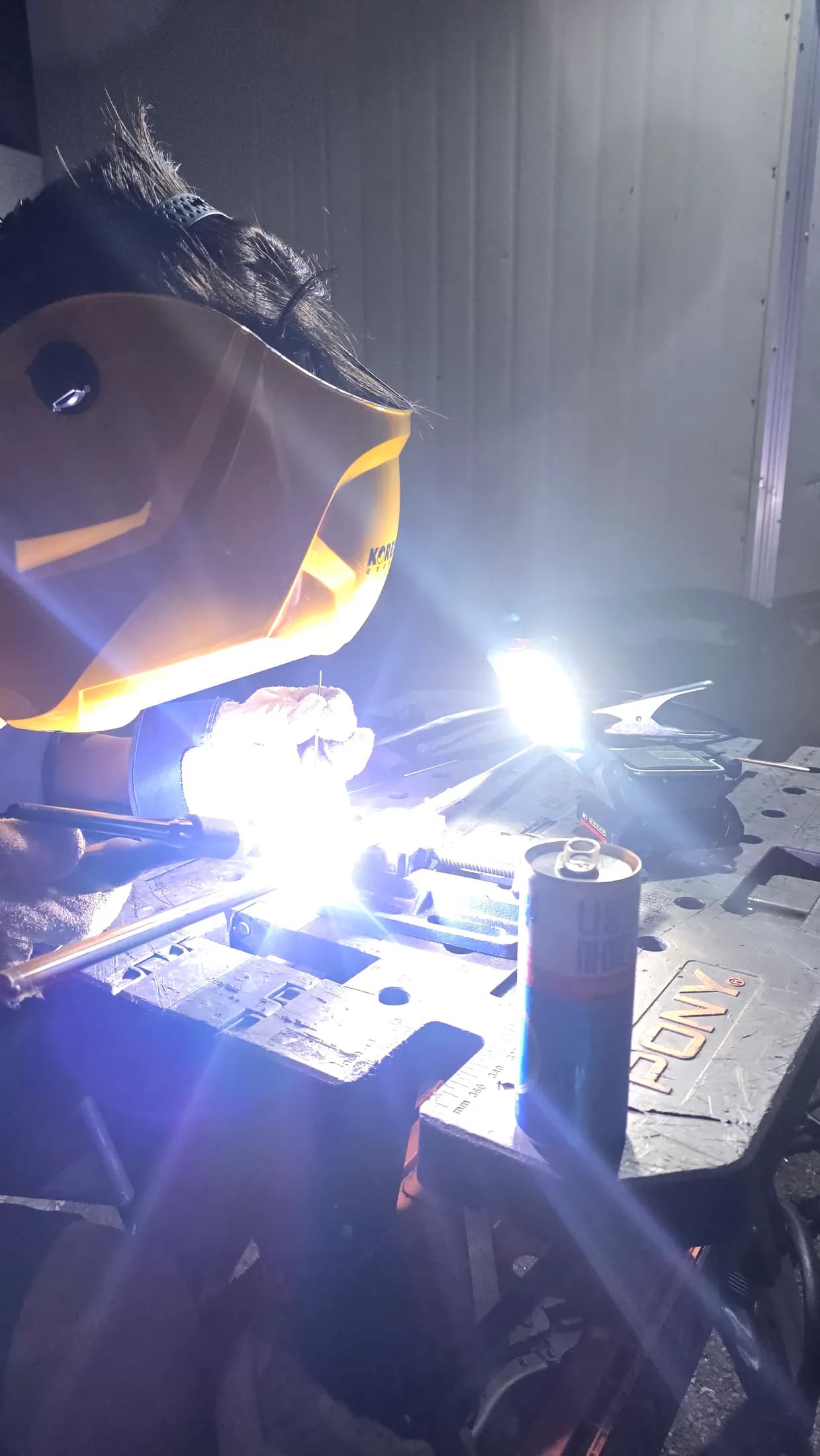 Person welding a metal component on a workbench during late-night fabrication.