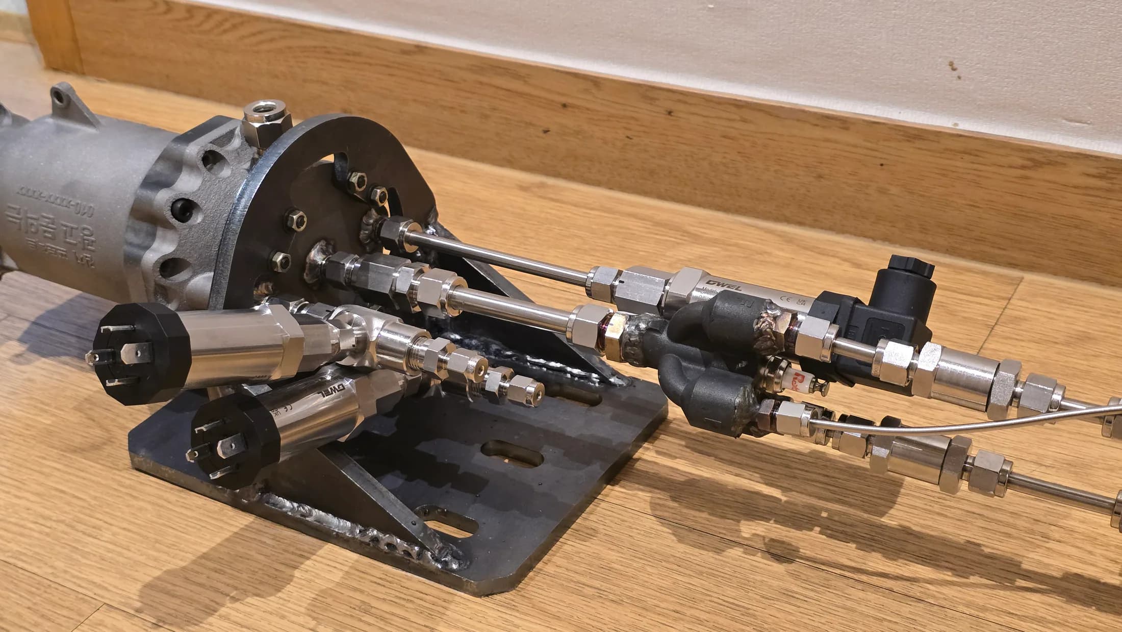 Close indoor view of the assembled injector and feed-line hardware mounted on a base.