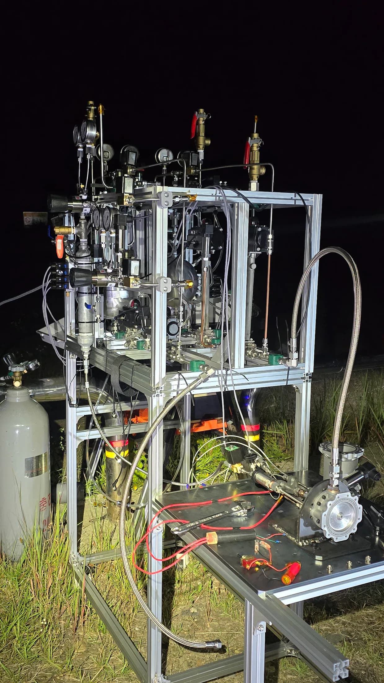 Engine test stand ready at night with frame, bottles, tubing, and electronics visible.