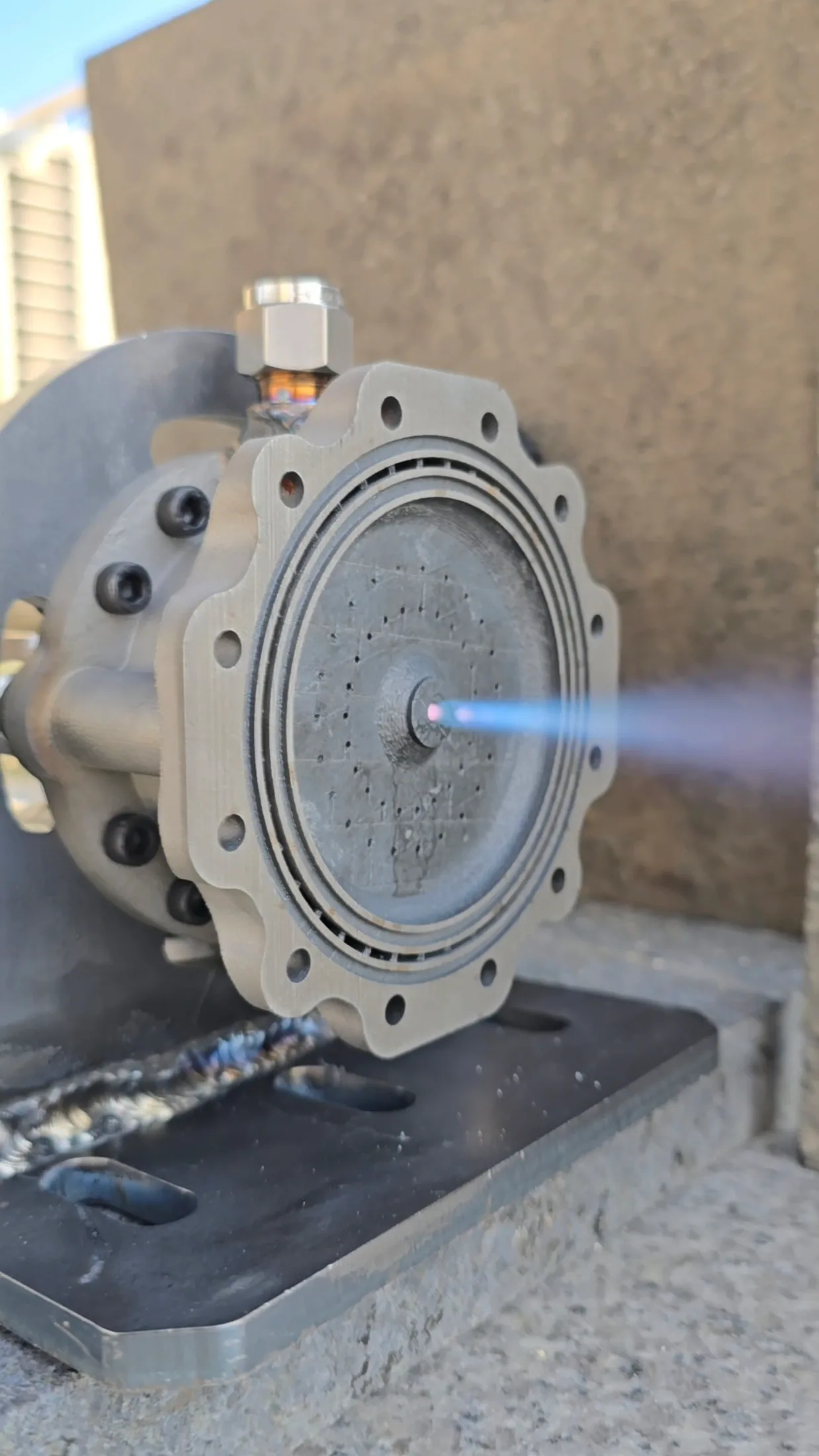 Close-up of the igniter face producing a short blue flame during a firing test.