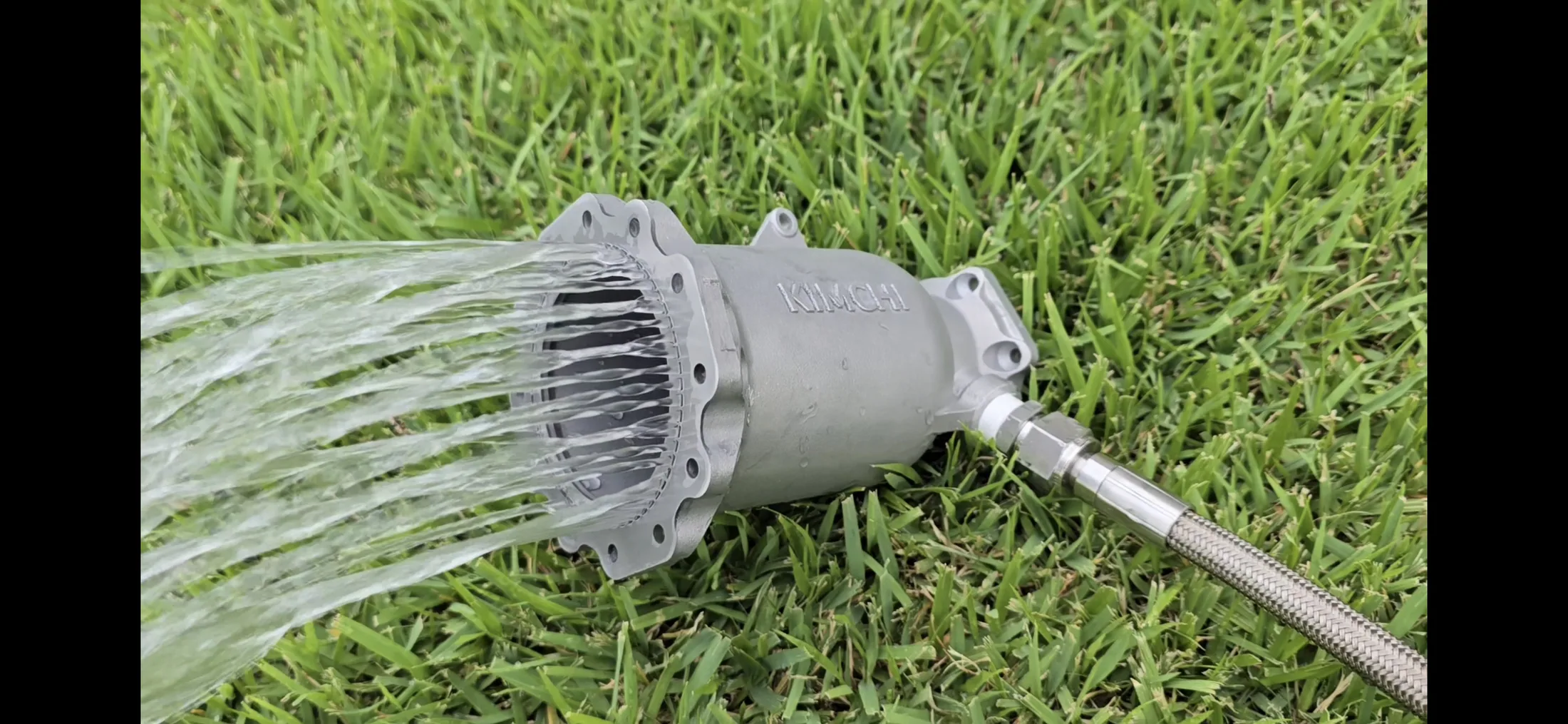 Cylindrical engine component on grass spraying multiple water streams from its outlet.